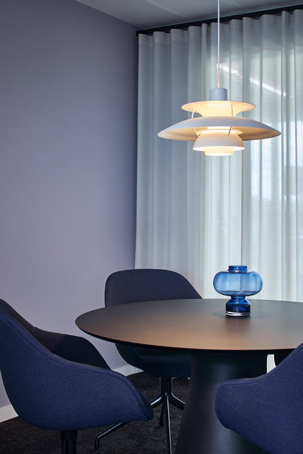Ein stilvoller Besprechungsbereich bei Arethia mit einem runden, dunklen Tisch und bequemen Polstersesseln in Dunkelblau. Über dem Tisch hängt eine ikonische weiße Design-Pendelleuchte. Ein heller Vorhang im Hintergrund sorgt für eine wohnliche Atmosphäre.
