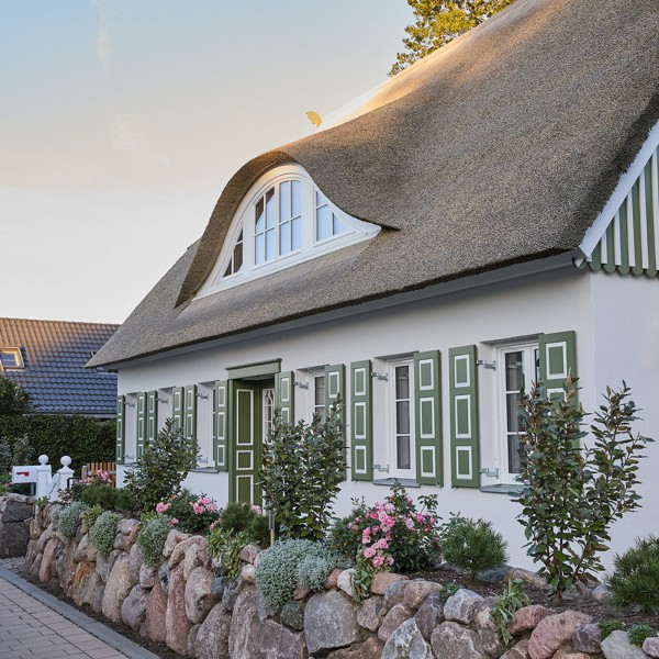 Reetgedecktes Ferienhaus Wustrow mit weißen Wänden und grünen Fensterläden.