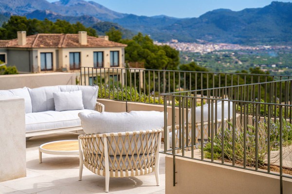 Eine sonnige Terrasse auf Mallorca mit hochwertigen Outdoormöbeln. Das helle Sofa und die Sessel mit Kordelflechtung bieten einen weiten Blick über die mediterrane Landschaft und die umliegenden Berge.