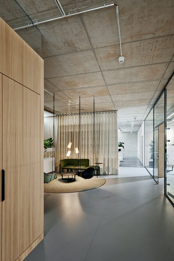 Referenzfoto: Eine der Lounges von Ramboll Berlin mit Schaukelsessel Swinging Eames, grünem Sofa und Holz-/Glaswänden.