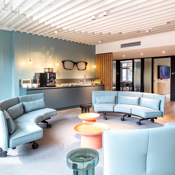 Lounge-Bereich der Fielmann Group mit geschwungenen Sofas und Brillen-Deko.