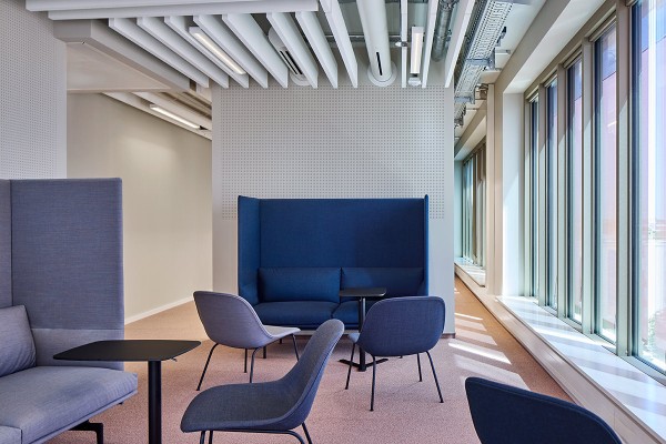 Ein einladender Aufenthaltsbereich im MIN Forum + Informatik Hamburg bietet blaue Sofas mit hohen akustischen Rückenlehnen und dazu passende Sessel. Kleine schwarze Laptoptische ergänzen die Sitzgruppen. Eine lange Fensterfront sorgt für viel Tageslicht.