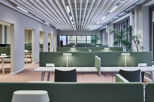 Der großzügige Lernbereich im MIN Forum + Informatik Hamburg ist mit langen Schreibtischreihen ausgestattet. Grüne Trennwände und dezente Tischleuchten schaffen ruhige Einzelarbeitsplätze. Eine Lamellendecke und Zimmerpflanzen ergänzen das Design.