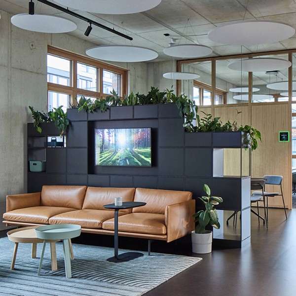 Lounge-Bereich bei Visual Art mit Ledersofa von Muuto, Bepflanzung und runden Akustikelementen.
