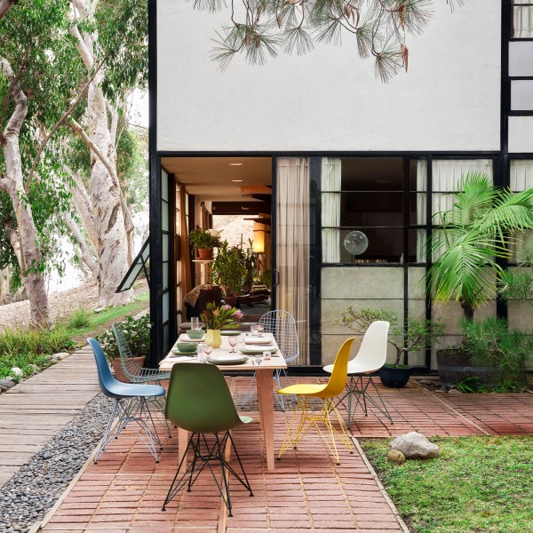 Eames Plastic Chairs und Wire Chairs um einen Holztisch auf einer Terrasse.
