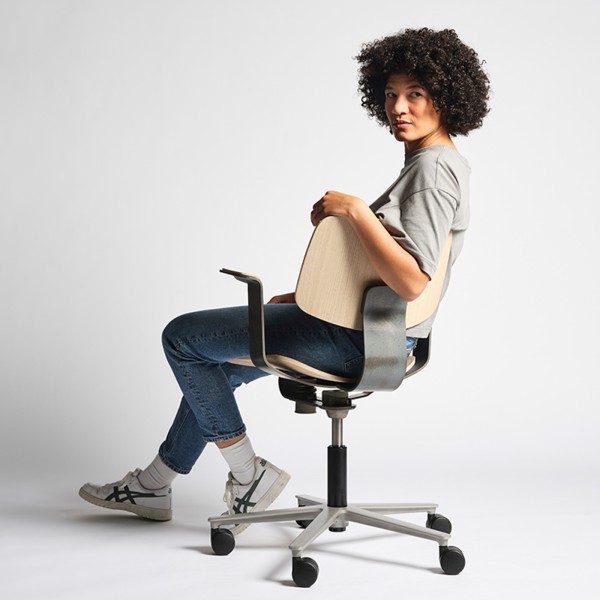 Junge Frau auf einem Wilkhahn WiChair in Holz und Schwarz vor hellem Hintergrund.