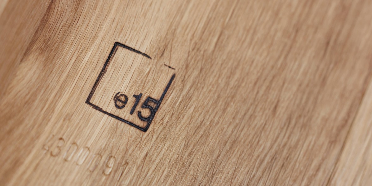 Die Nahaufnahme zeigt das in hellem Eichenholz eingebrannte Logo der Designmarke e15. Neben dem quadratischen Brandstempel ist eine eingeprägte Seriennummer auf der Holzoberfläche zu erkennen.