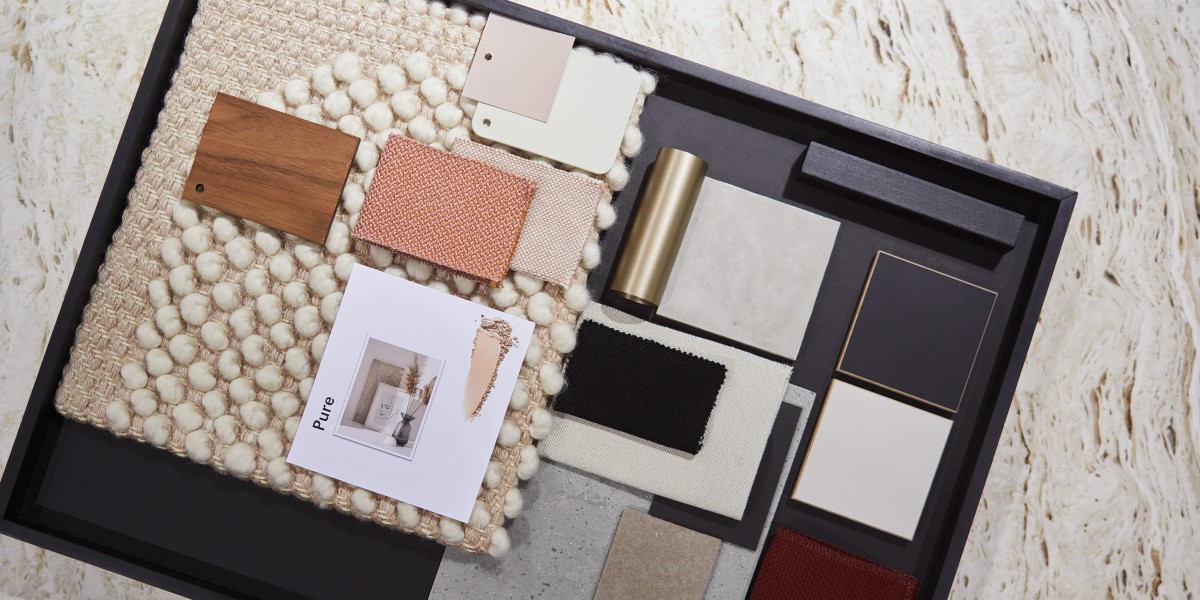 In einem dunklen Tablett präsentiert gärtner eine Materialcollage für Kunden. Neben Holzmusterplättchen und Stoffproben sind Teppichmuster, Metallakzente sowie Farbkarten arrangiert.