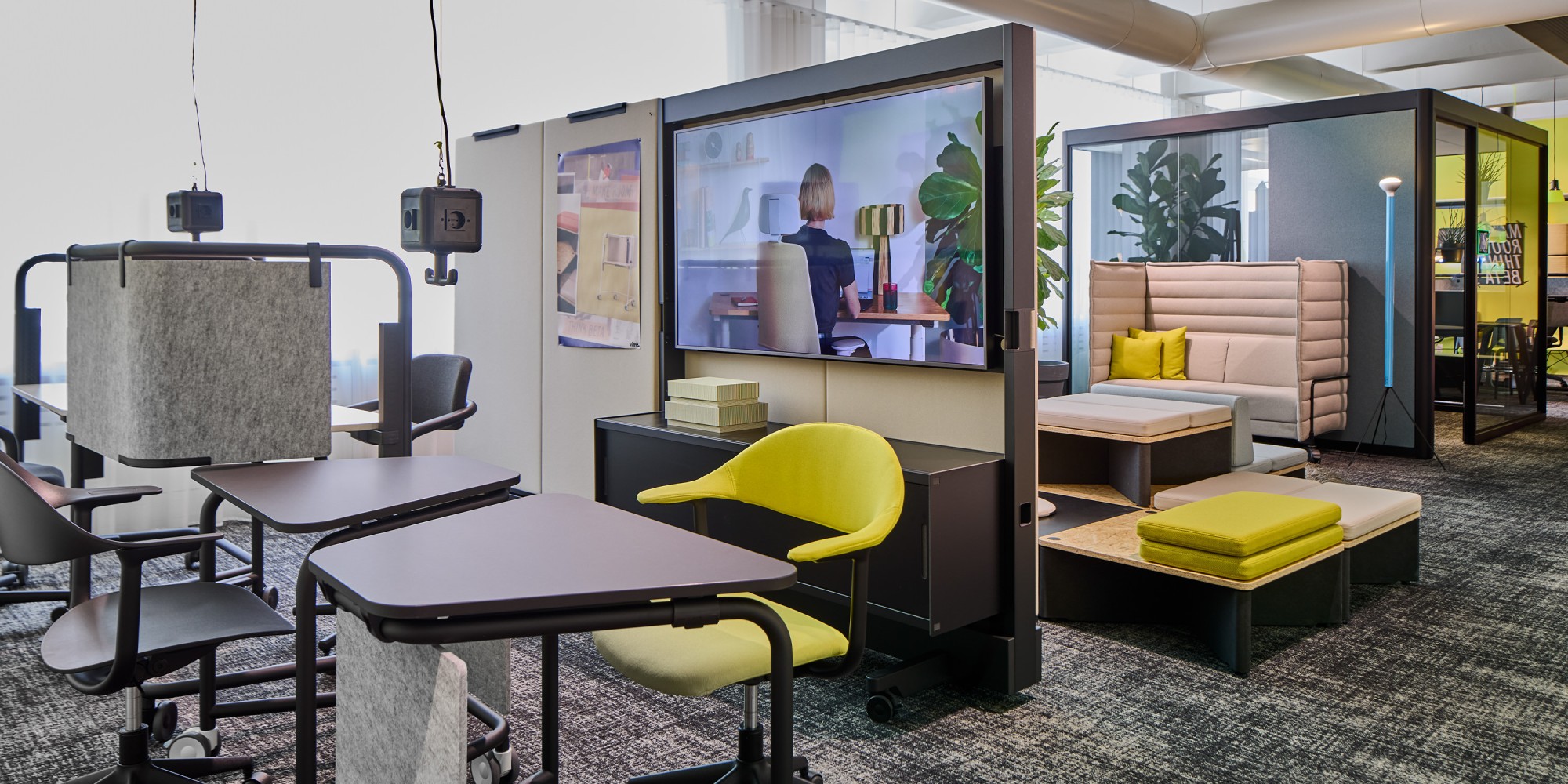 Ein Einblick in die dynamische Vitra THINK BETA Zone im gärtner Showroom. Mobile Tische und Drehstühle im Vordergrund treffen auf ein zentrales Medienelement sowie eine dahinterliegende, flexible Lounge- und Meeting-Area.
